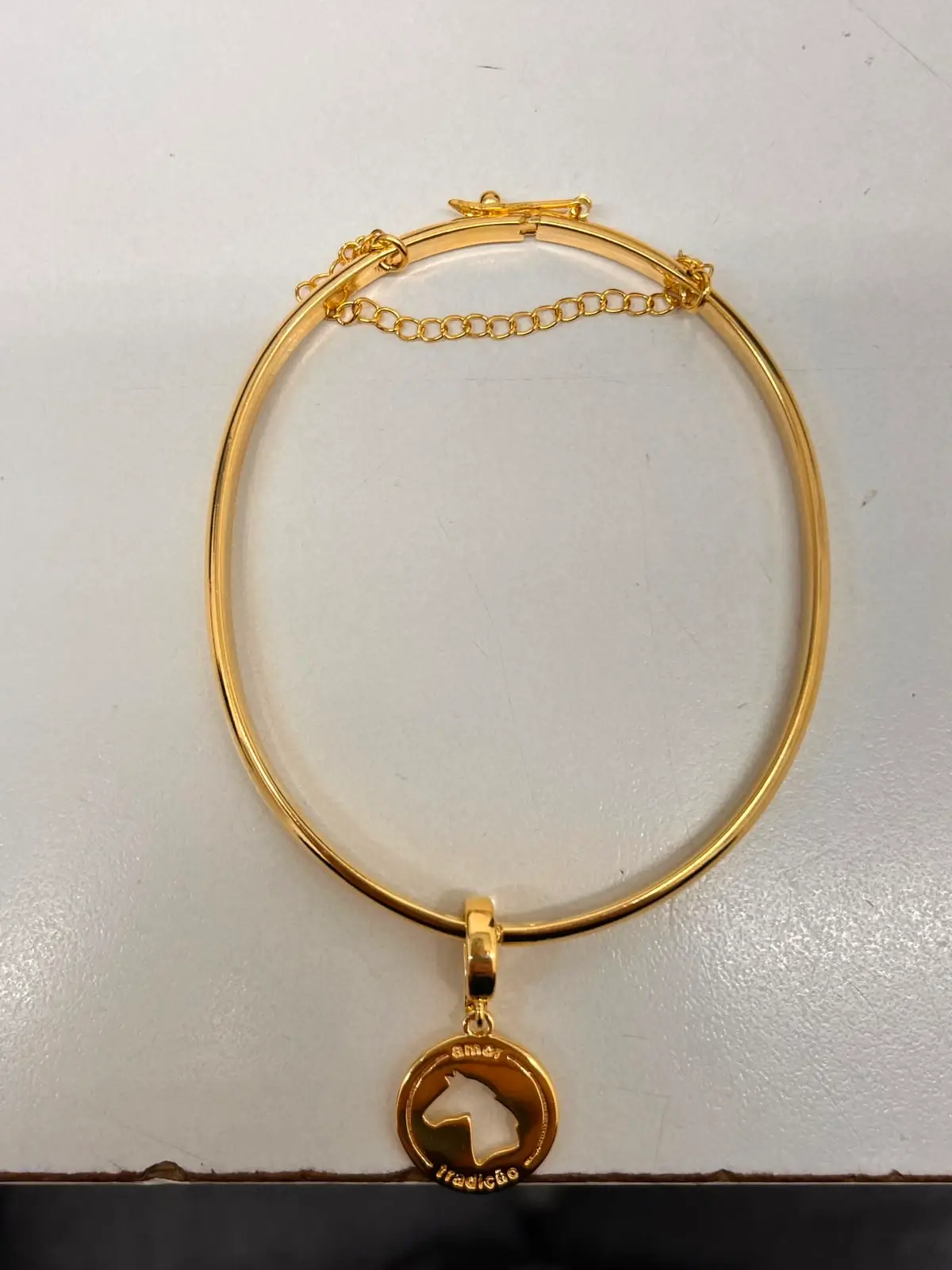 Bracelete dourado fotografado no celular, sobre a mesa de casa